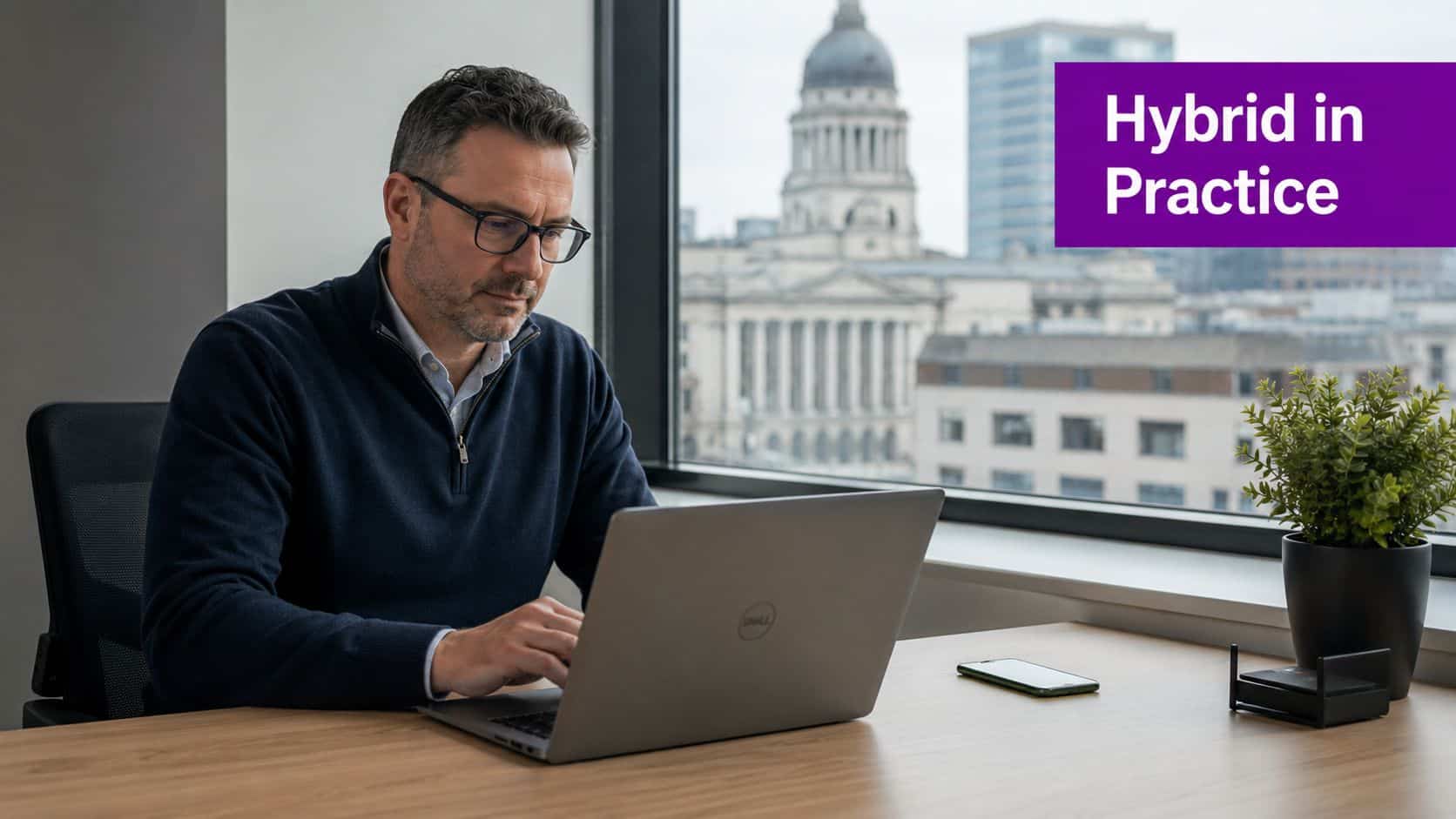 A professional man with glasses working on a laptop in a modern office with city views.
